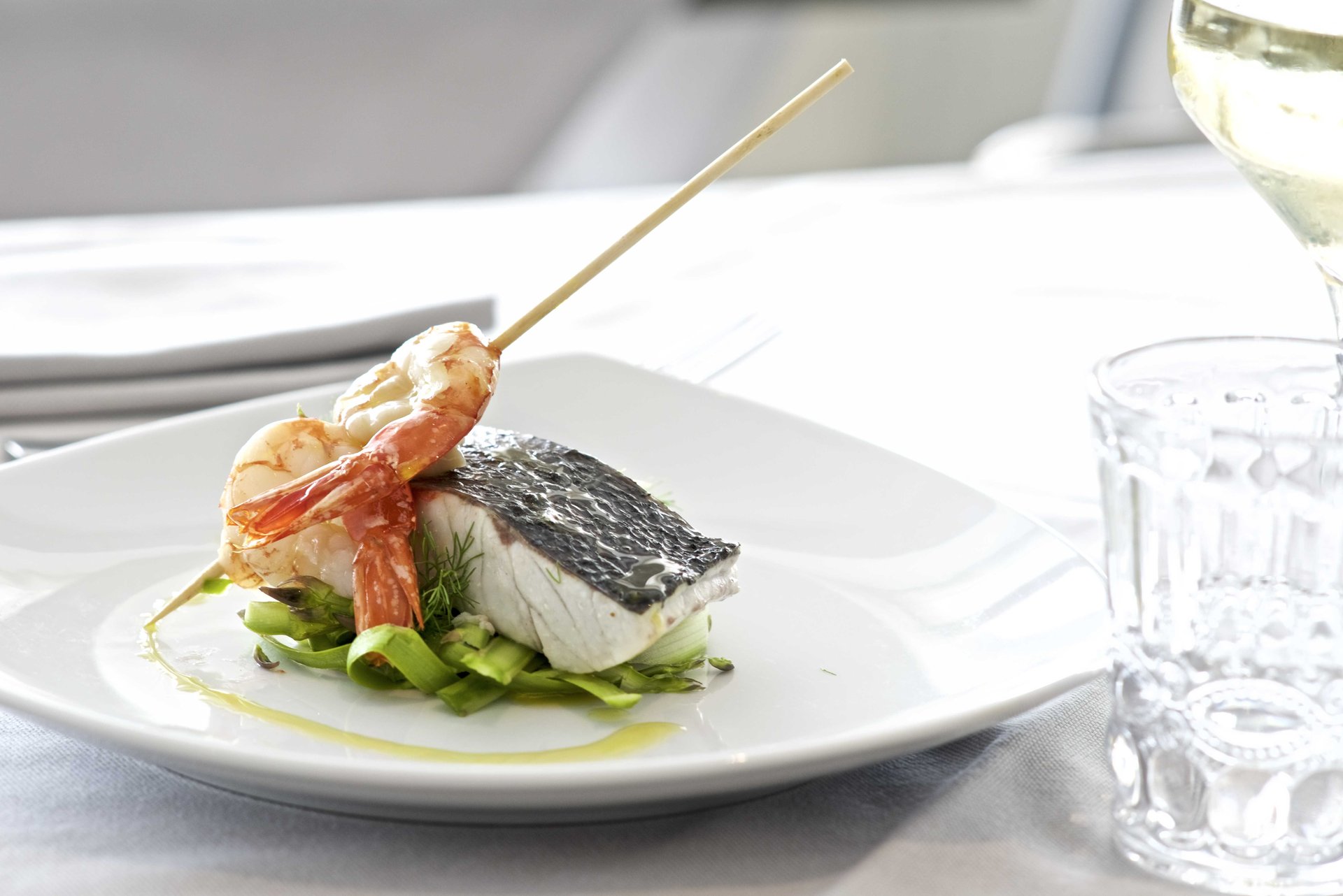 Trancio di pesce con la pelle e spiedino di gambero su verdure, calice e bicchiere, Centosedici