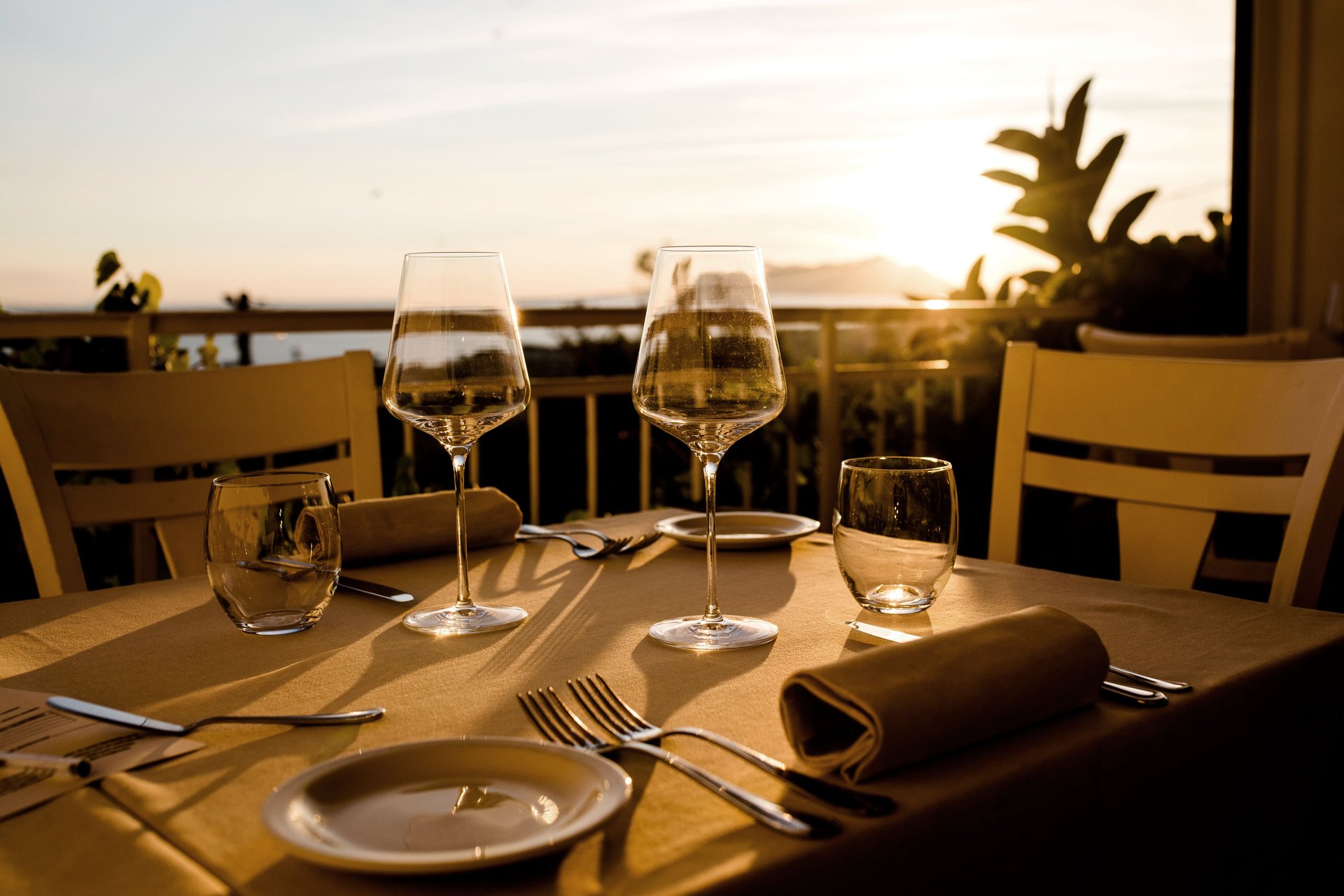 Tavola apparecchiata sulla terrazza al tramonto, calici, ringhiera e sole basso dietro, Il Granchio