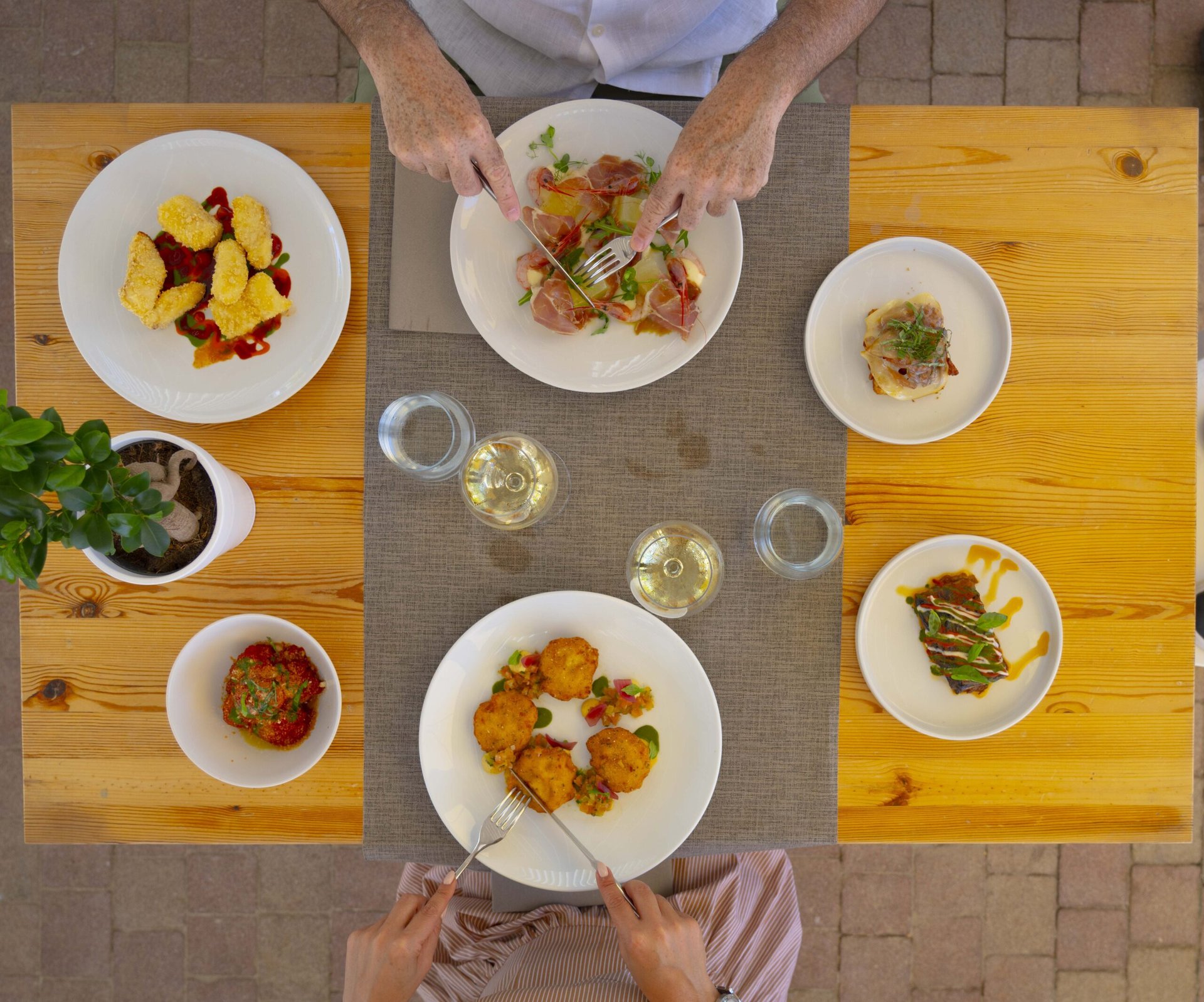 Tavolo di legno dall'alto: due commensali, sei piatti di assaggi, due calici di bianco, Le Palme Village / Zero Food Experience