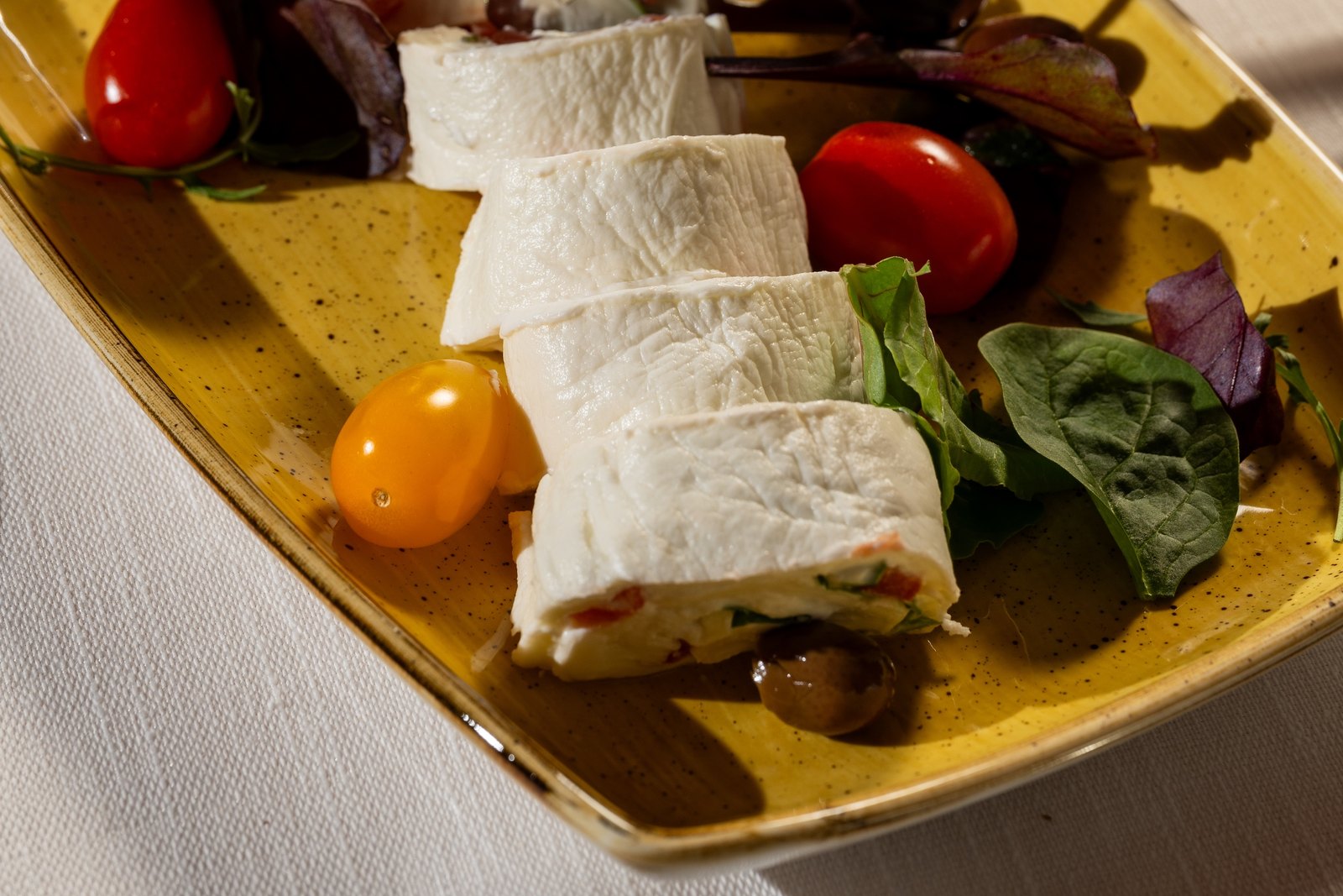 Rotolini di formaggio bianco su un piatto giallo, con pomodorini e insalata