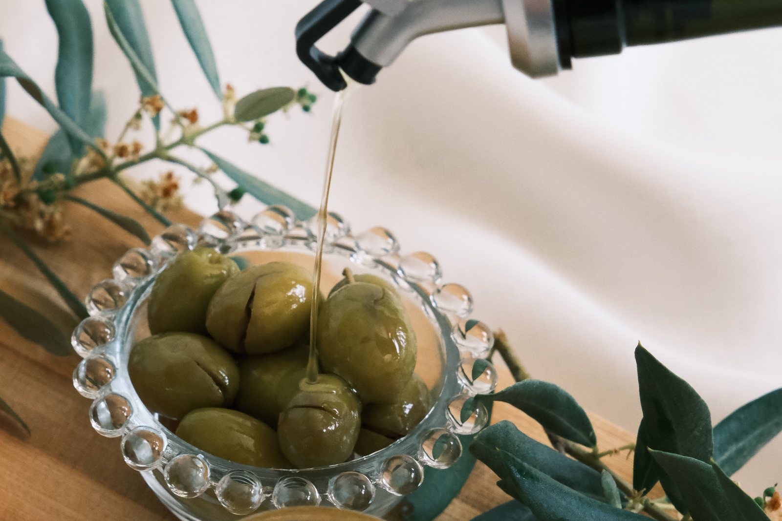 Olio versato su una ciotola di olive verdi, con rami d'ulivo