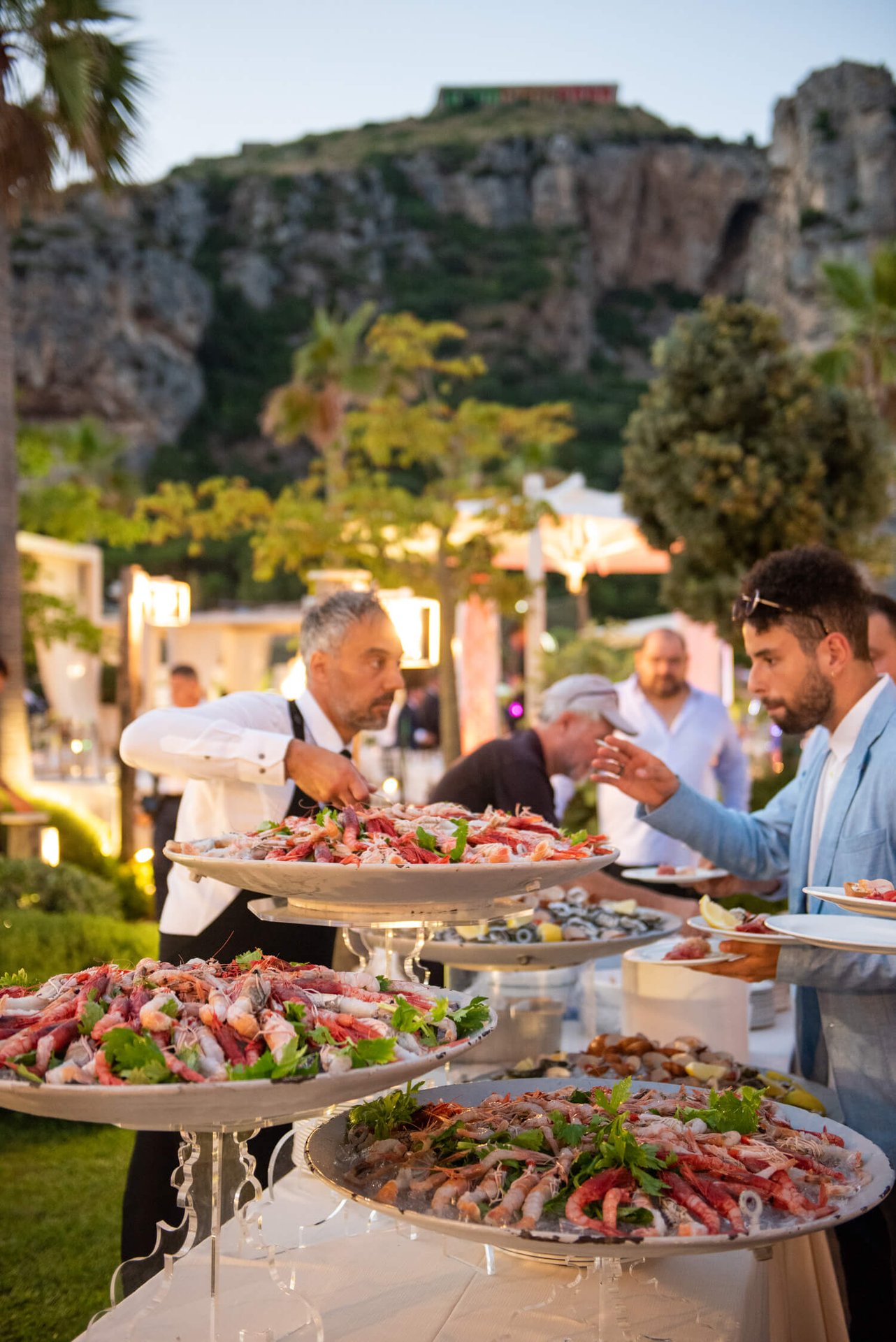 Cameriere e ospiti a un buffet all'aperto con crostacei crudi, Monte Sant'Angelo col Tempio di Giove dietro, Ristorante Grappolo D’Uva Ricevimenti