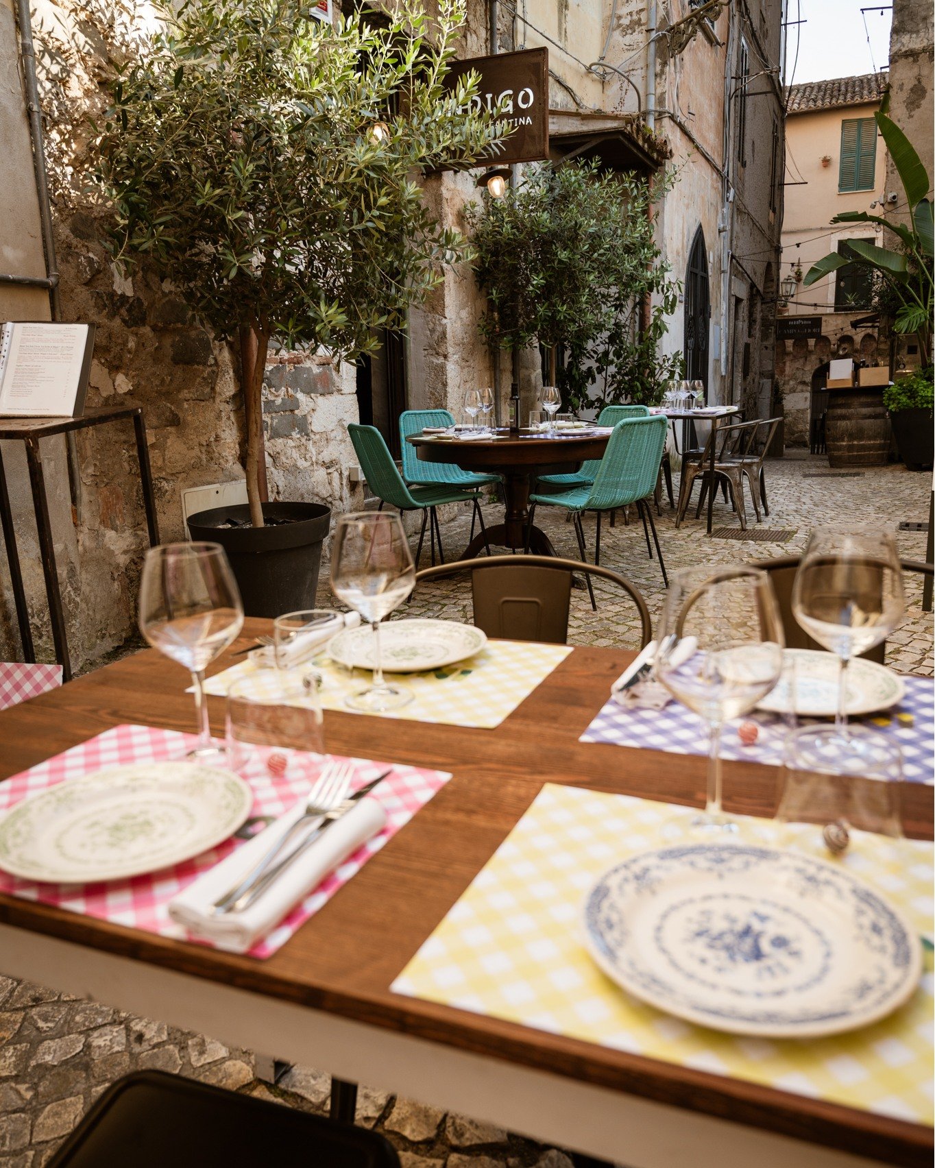Dehors nel vicolo in pietra del centro storico, tavolo apparecchiato in primo piano, insegna del locale dietro, Ristorante Indigo