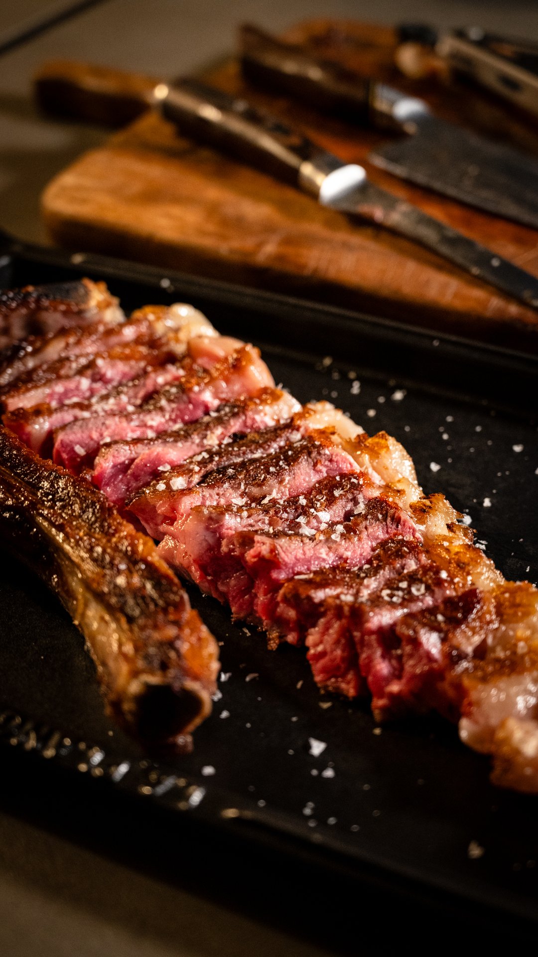 Bistecca con l'osso tagliata a fette su piastra nera, coltelli e tagliere, Ristorante Indigo