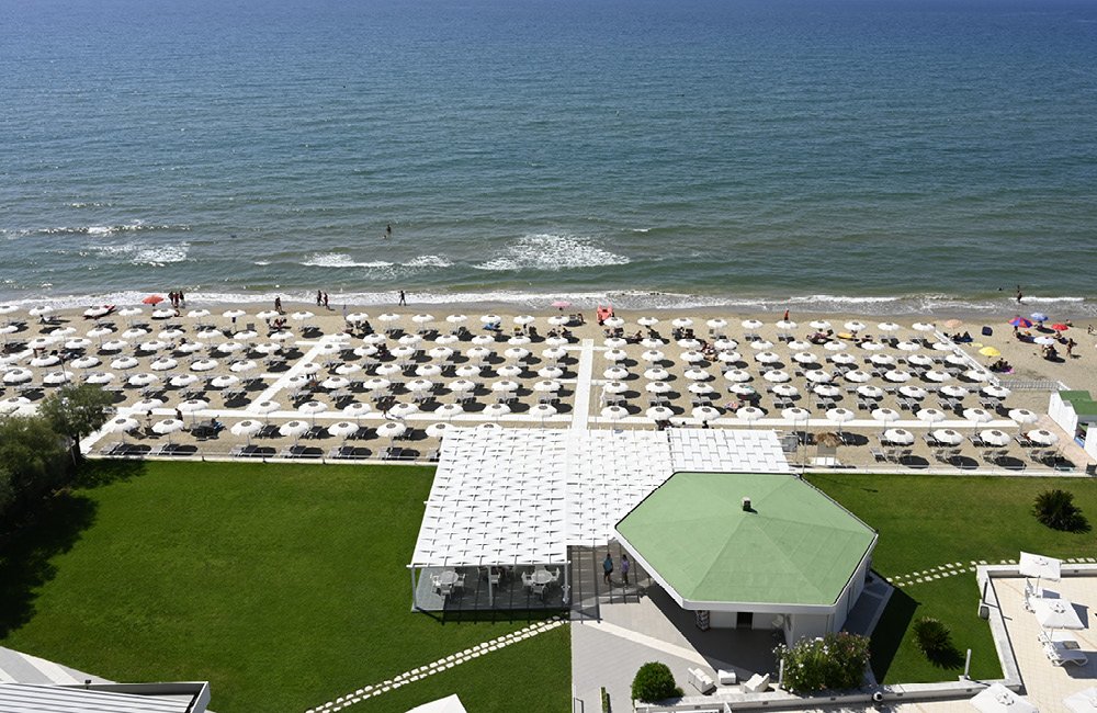 Vista dall'alto: prato, padiglione, file di ombrelloni sulla spiaggia e mare, Torre del Sole